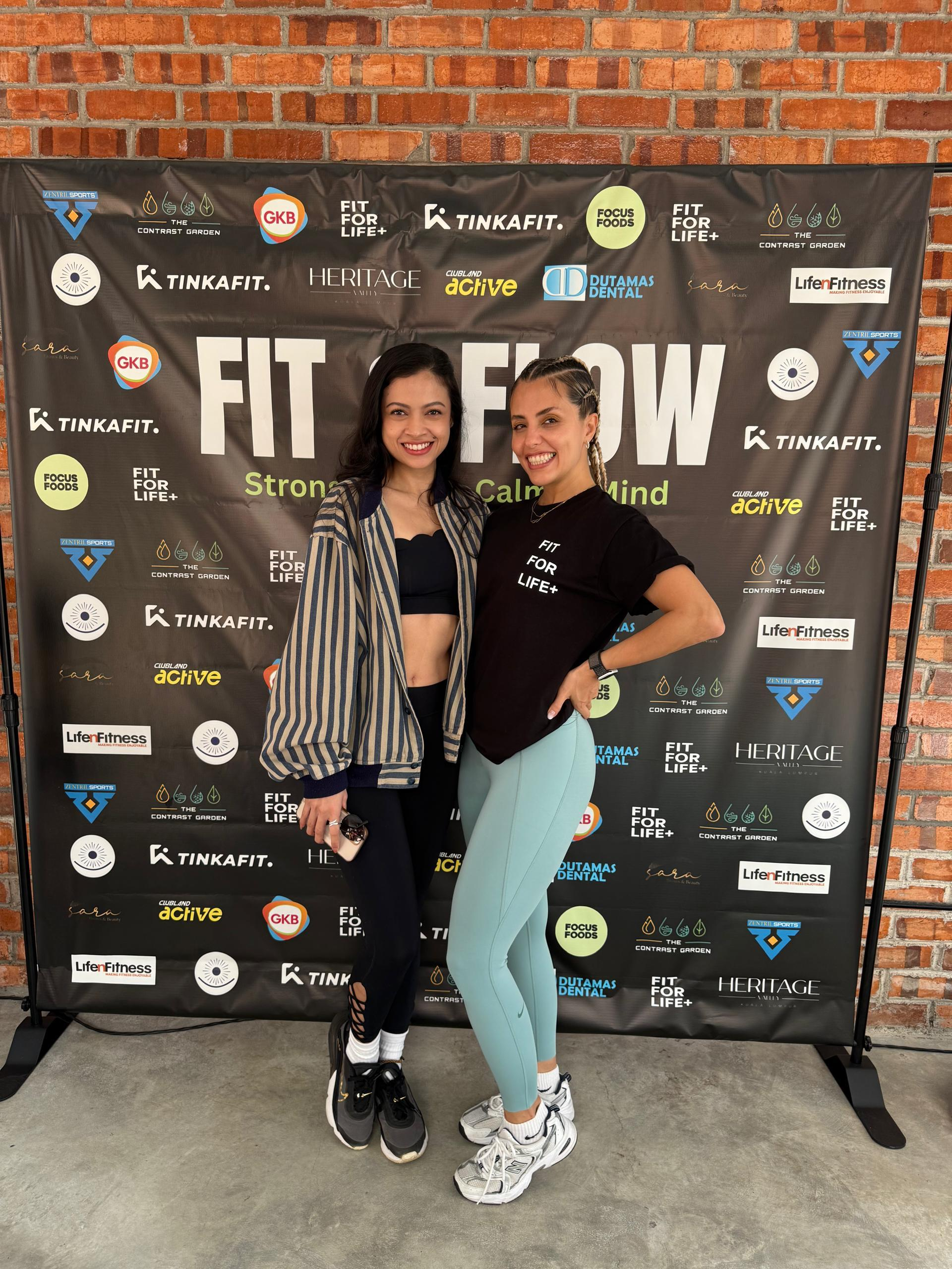 Two participants posing together at a wellness event backdrop