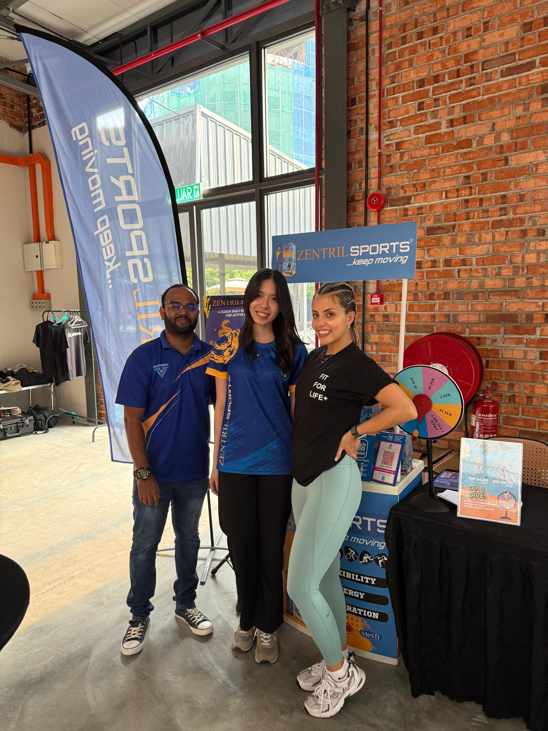 Three participants beside a promotional wellbeing booth and prize wheel